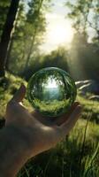 Hand holding a transparent green globe reflecting nature in a forest setting photo
