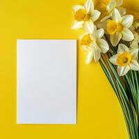 Bright yellow background with daffodils and blank sheet of paper for creative projects photo