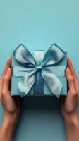 Gift wrapped in light blue with satin bow held by hands against a vibrant background photo