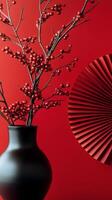Elegant arrangement of red berries in a black vase with a fan on a vibrant red background photo