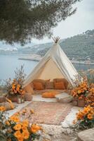 Cozy bohemian tent setup near the water with vibrant flowers and soft cushions in a scenic landscape photo
