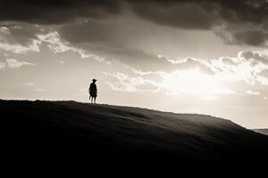 A lone man stands on a hill overlooking the sunset photo