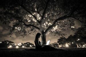 A woman sitting under a tree with a laptop photo