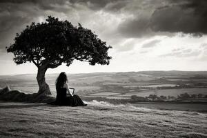 A woman sitting under a tree on a hill photo
