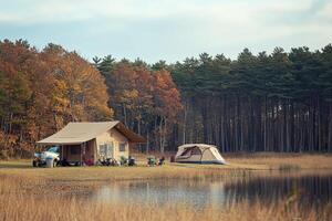 A tent and a camper are sitting on the shore of a lake photo