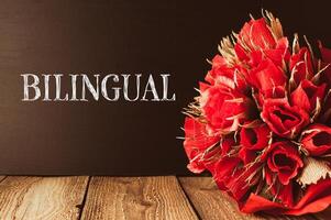 Bouquet of red roses is on a wooden table with the word bilingual photo
