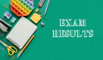 Exam results are written on a green background with a notebook, pens photo