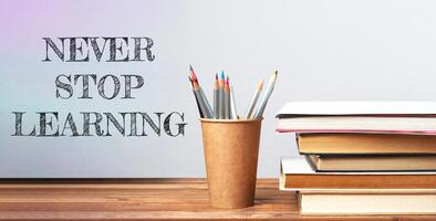 Never stop learning. A pencil holder with pencils sits on a table with a stack of books photo