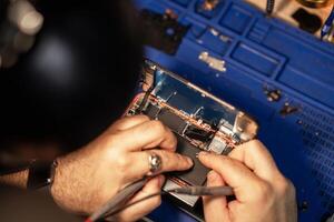 Technician performing smartphone battery repair in a workshop with tools and components while focused on detail photo