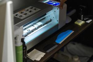 Operator uses a precise cutting plotter for hydrogel film preparation in a workshop setting during daylight hours photo