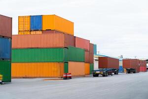 A large number of containers are stacked in a warehouse. The containers are of different colors, including green, yellow, and red. There are also trucks in the scene, with one truck being blue photo