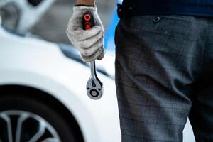 A man is holding a wrench and wearing gloves. He is standing next to a car. Concept of work and maintenance, as the man is likely a mechanic or a car enthusiast photo