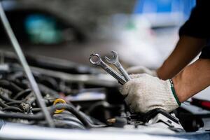 A mechanic is working on a car engine, holding a pair of wrenches in his hands. Concept of focus and determination as the mechanic works to fix the car photo