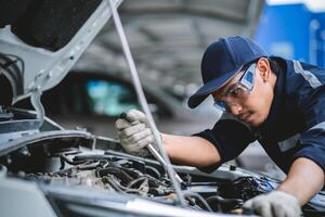 A man in a blue shirt and goggles is working on a car. He is using a jumper cable to jump start the car photo