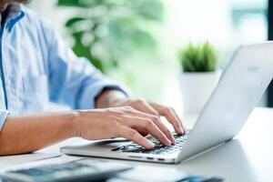 A man is typing on a laptop in front of a potted plant. Concept of productivity and focus, as the man is likely working on a task or project photo