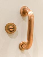 A close up of a copper handle on a white door photo