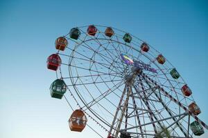 From below static ferris wheel against a clear blue sky, showcasing its symmetry and colorful patterns on the passenger cabins photo