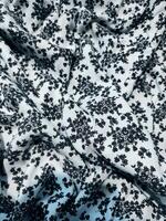 The pattern and background of the fabric is white with a small black flower motif photo