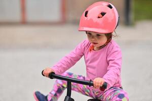 A little girl, dressed in a cute outfit and wearing a helmet, excitedly learning to ride her bike for the first time, filled with joy and determination. photo