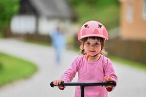 A little girl, dressed in a cute outfit and wearing a helmet, excitedly learning to ride her bike for the first time, filled with joy and determination. photo