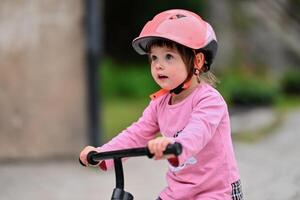 A little girl, dressed in a cute outfit and wearing a helmet, excitedly learning to ride her bike for the first time, filled with joy and determination. photo