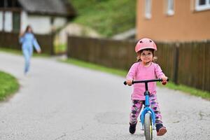 A little girl, dressed in a cute outfit and wearing a helmet, excitedly learning to ride her bike for the first time, filled with joy and determination. photo