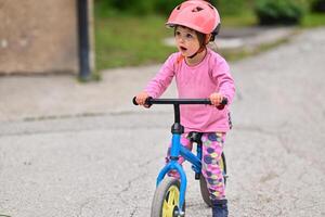 A little girl, dressed in a cute outfit and wearing a helmet, excitedly learning to ride her bike for the first time, filled with joy and determination. photo