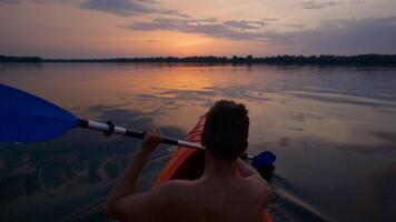 A man kayaks on a calm river towards the sunset. He skillfully rowing oar. Beautiful nature of the evening river. Super Slow Motion video