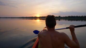 A man kayaks on a calm river towards the sunset. He skillfully rowing oar. Beautiful nature of the evening river. Super Slow Motion video
