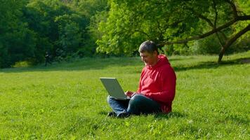 Man working on laptop in summer forest At The Sunny Day. Busy freelance worker is tired and wants to rest. Freelancer Remote Work Concept. 4K video