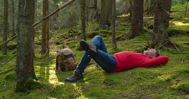 Man in nature. Outdoor travel concept. Tourist guy resting on moss in a beautiful forest. Slow motion video