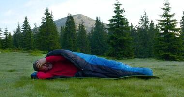 Bearded man sleeping in a sleeping bag on a beautiful meadow in the mountains. Travel concept. Ultra 4K 50 fps slow motion video