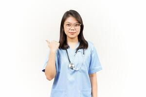 Showing and Pointing Product With Thumb Of Asian Young Doctor Isolated On White Background photo