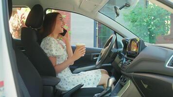 Happy cheerful smiling Caucasian woman female girl driver owner using mobile phone talking smartphone call chatting with friends drinking coffee inside new automobile car rental transport rent service video