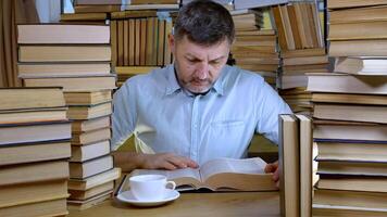A bearded man reads a book in the library. Stacks of books and cup of tea on table. Concept of Reading and Education. photo
