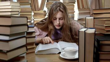 A girl reads a book in the library. Stacks of books and cup of tea on table. Concept of Reading and Education. photo
