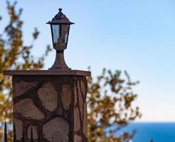 Small lamp lamp on a stone pillar. In the background a tree and blue sea. High quality photo. photo
