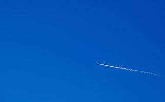 Flight of an airplane with a white trail diagonally against a clear blue sky. For text. photo