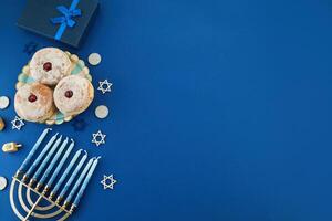 Jewish holiday Hanukkah concept. Frame of traditional jelly donuts and menorah on dark blue background photo