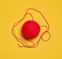 Ball of red woolen thread on yellow background, top view photo