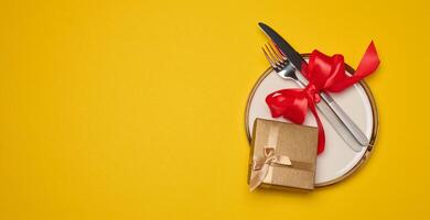 Round plate and tied fork with knife on yellow background, festive table setting photo