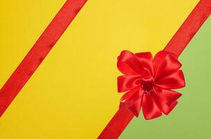 Tied bow made of red silk ribbon on green yellow background, decor for a gift photo