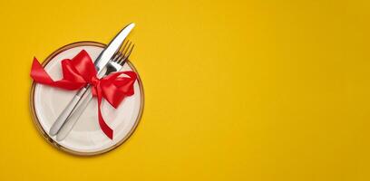 Round white plate and tied with red bow view with knife on yellow background, festive table setting photo