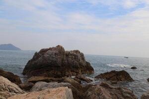 In the sea, there is an island with large rocks on it and boats in front of them photo