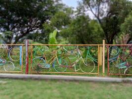 Colorful fence made from old bicycles. The unique fence is set against a backdrop of trees and lush greenery. photo