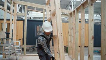 Carpenter in uniform walks with frame through unfinished prefabricated modular house in construction site video
