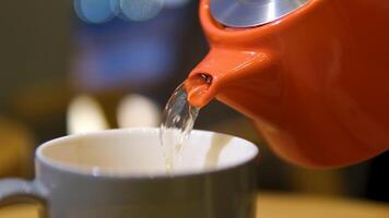 Making hot tea on the kitchen table. Boiling water is poured from the kettle into a cup with a tea bag. Transparent cup of freshly brewed tea on the kitchen table on a sunny day. video