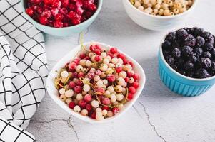 Frozen red and white currants in a bowl and other berries on the table photo