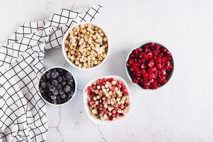 Assorted frozen red, white and black berries in bowls on table top view photo