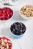 Frozen blackcurrants in a bowl and other berries on the table vertical view photo